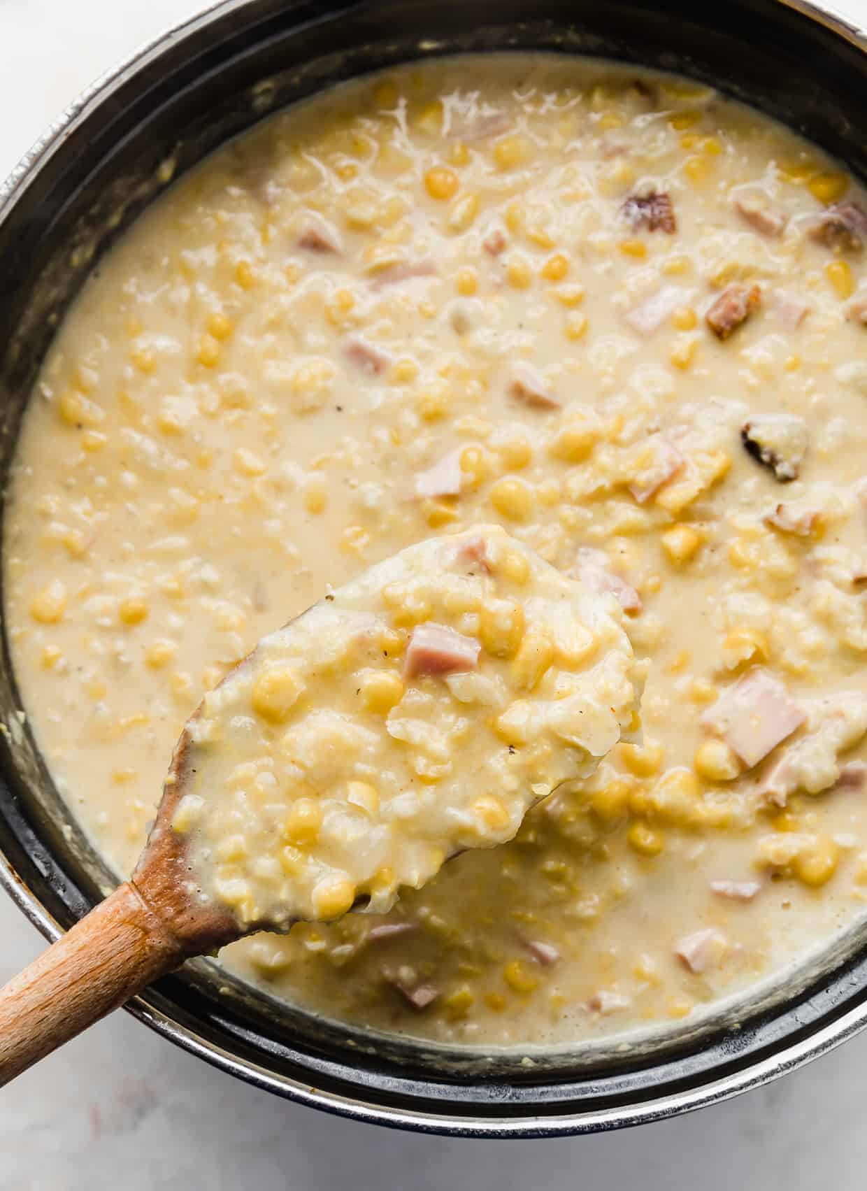 A wooden spoon scooping up homemade Ham and Corn Chowder.