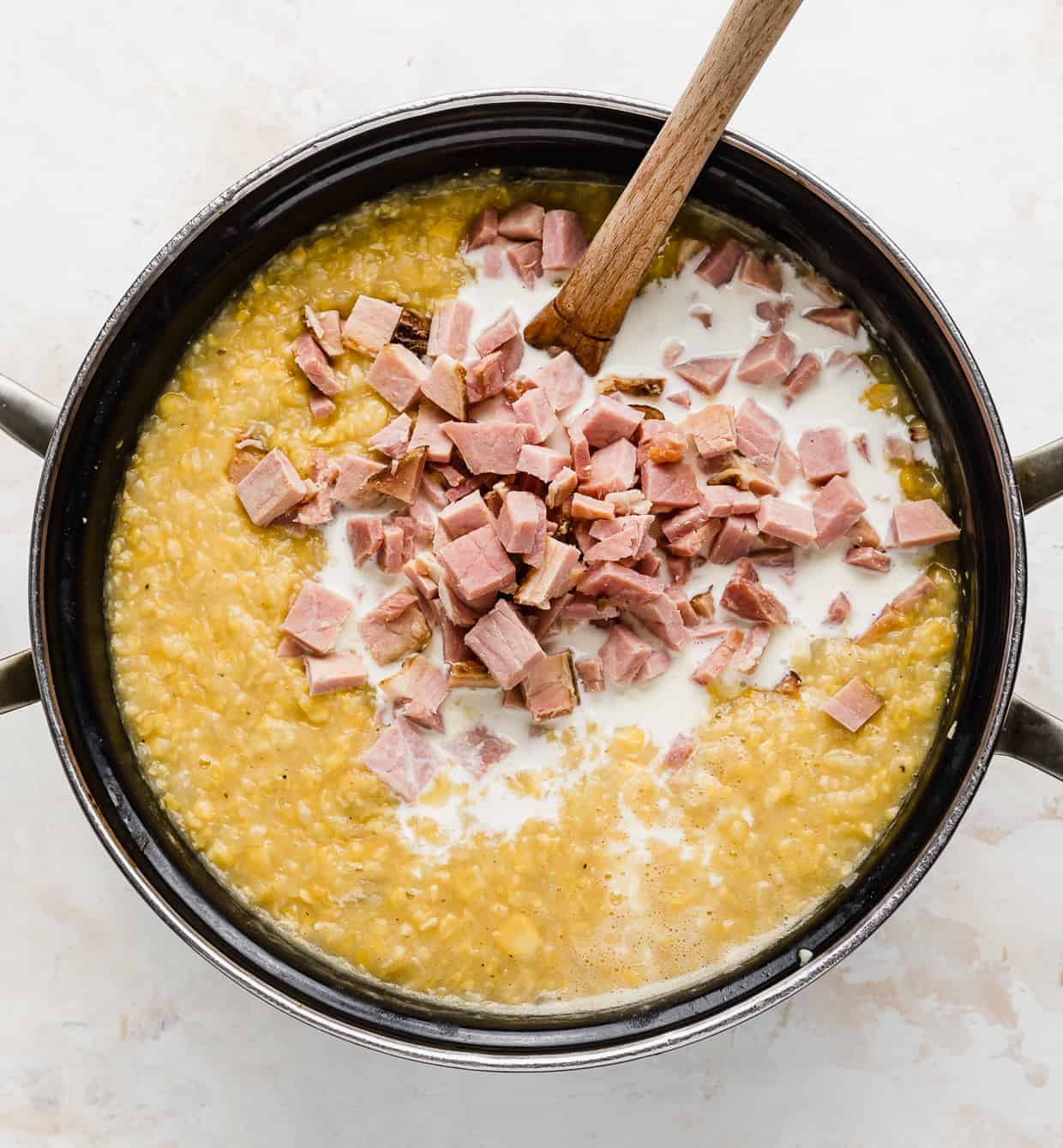 A large pot full of corn chowder, with diced ham and heavy cream placed overtop of the chowder.