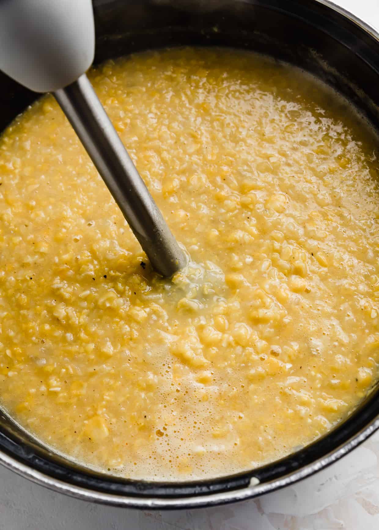 An immersion blender in a large pot full of cooked corn and potatoes for making Ham and Corn Chowder.