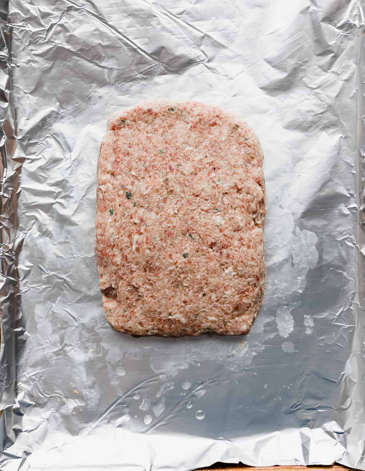 Raw lamb gyro meat on a foil lined baking sheet, shaped in a rectangle. 