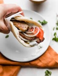 A hand holding up a greek lamb gyro in a flat bread.