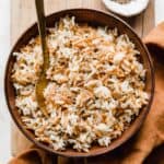 Orzo Rice in a brown bowl on a wooden cutting board.