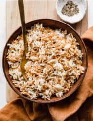 Orzo Rice in a brown bowl on a wooden cutting board.