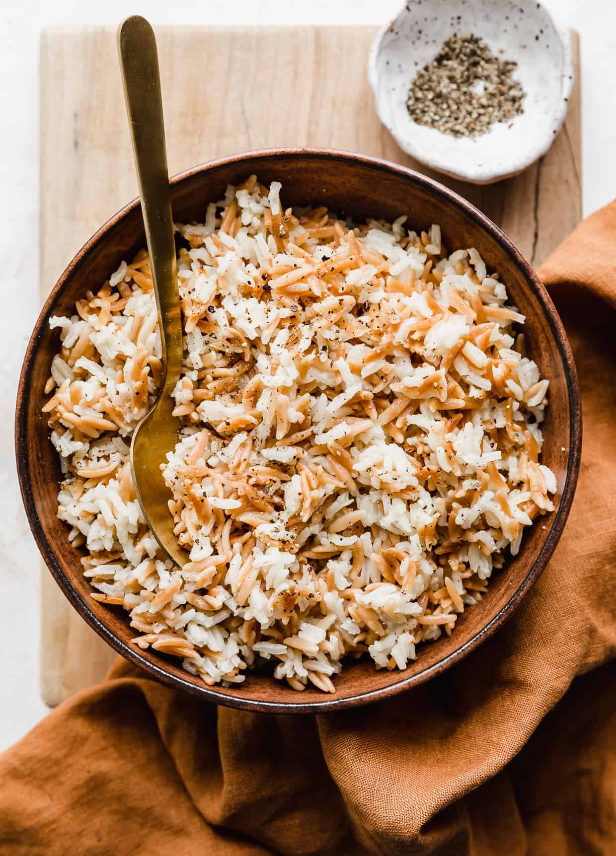 Orzo Rice in a brown bowl on a wooden cutting board. 
