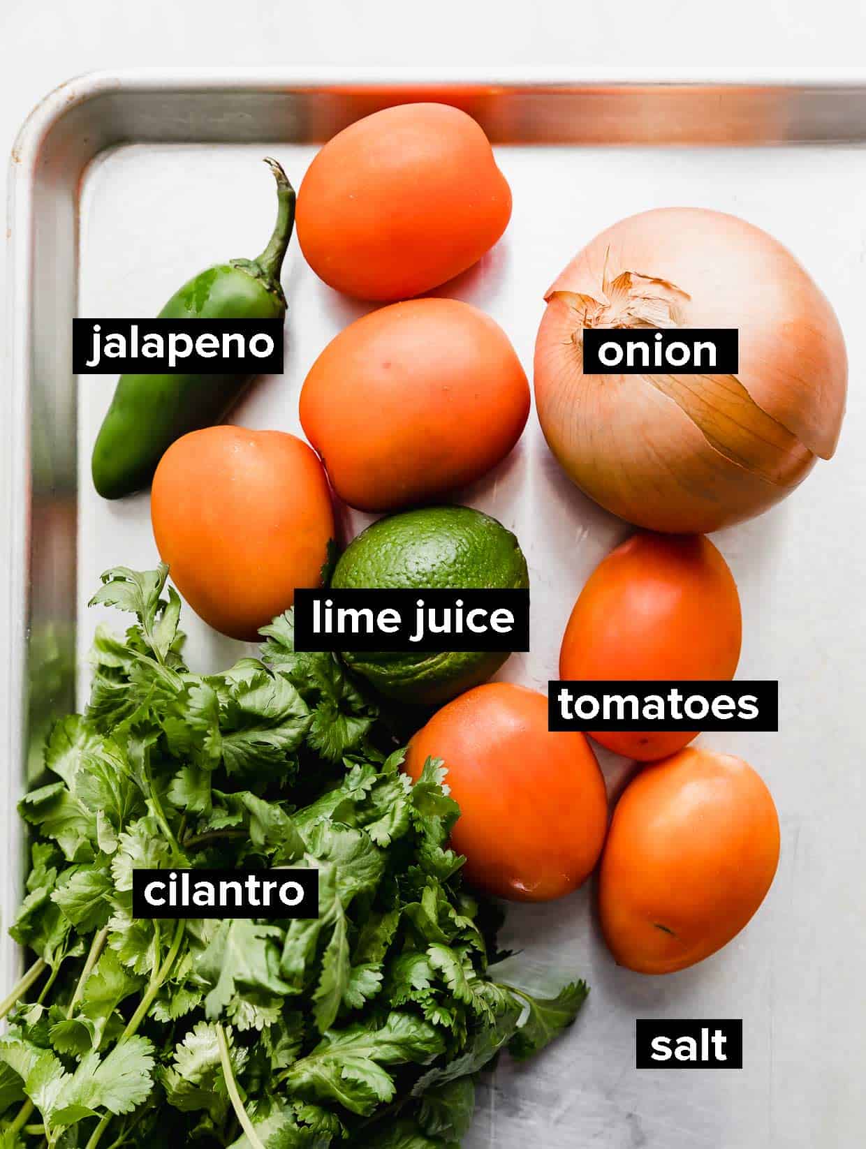 Ingredients used to make pico de Gallo on a silver baking sheet. 