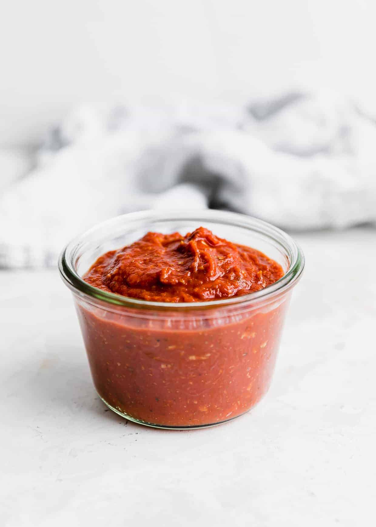 A glass jar full of Pizza Sauce from Tomato Paste against a white background. 