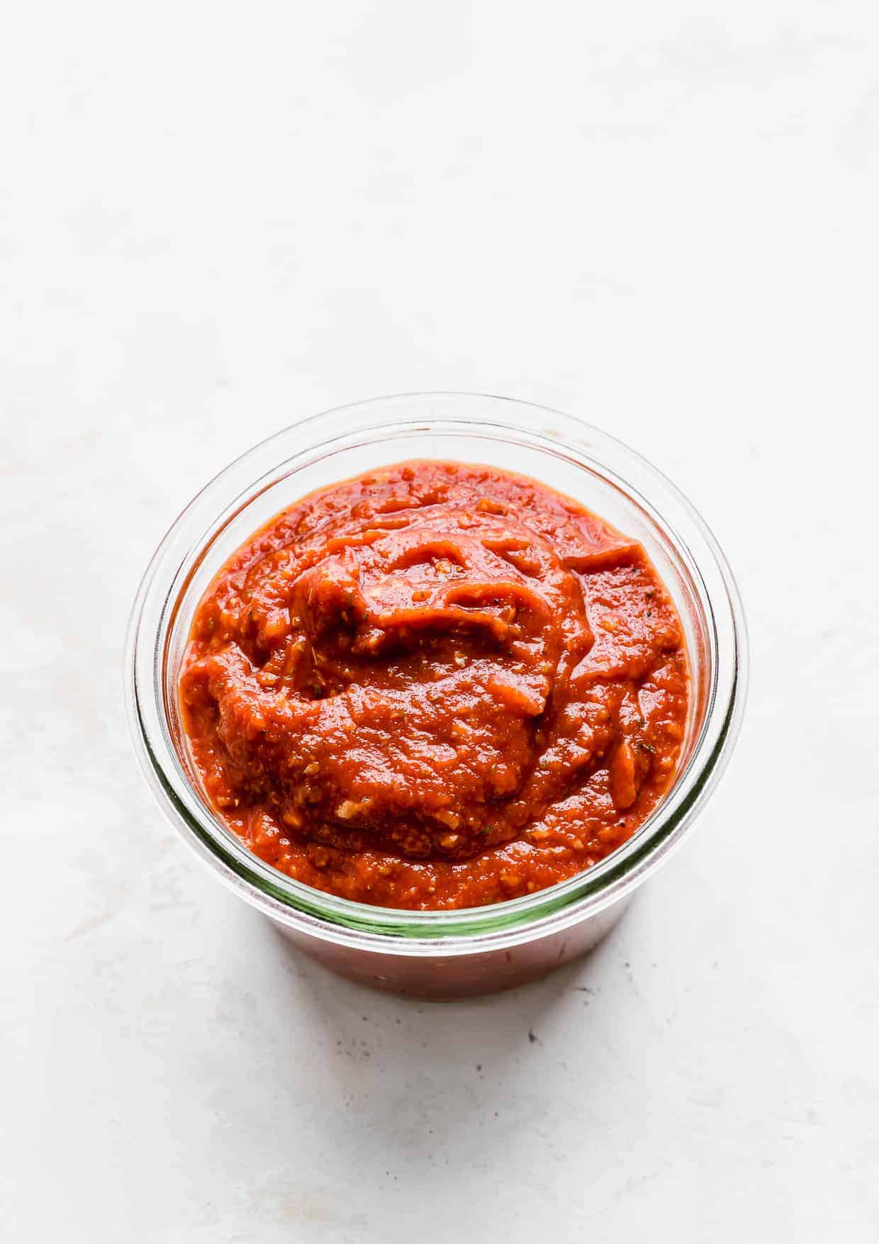 A jar of tomato paste pizza sauce against a white background.