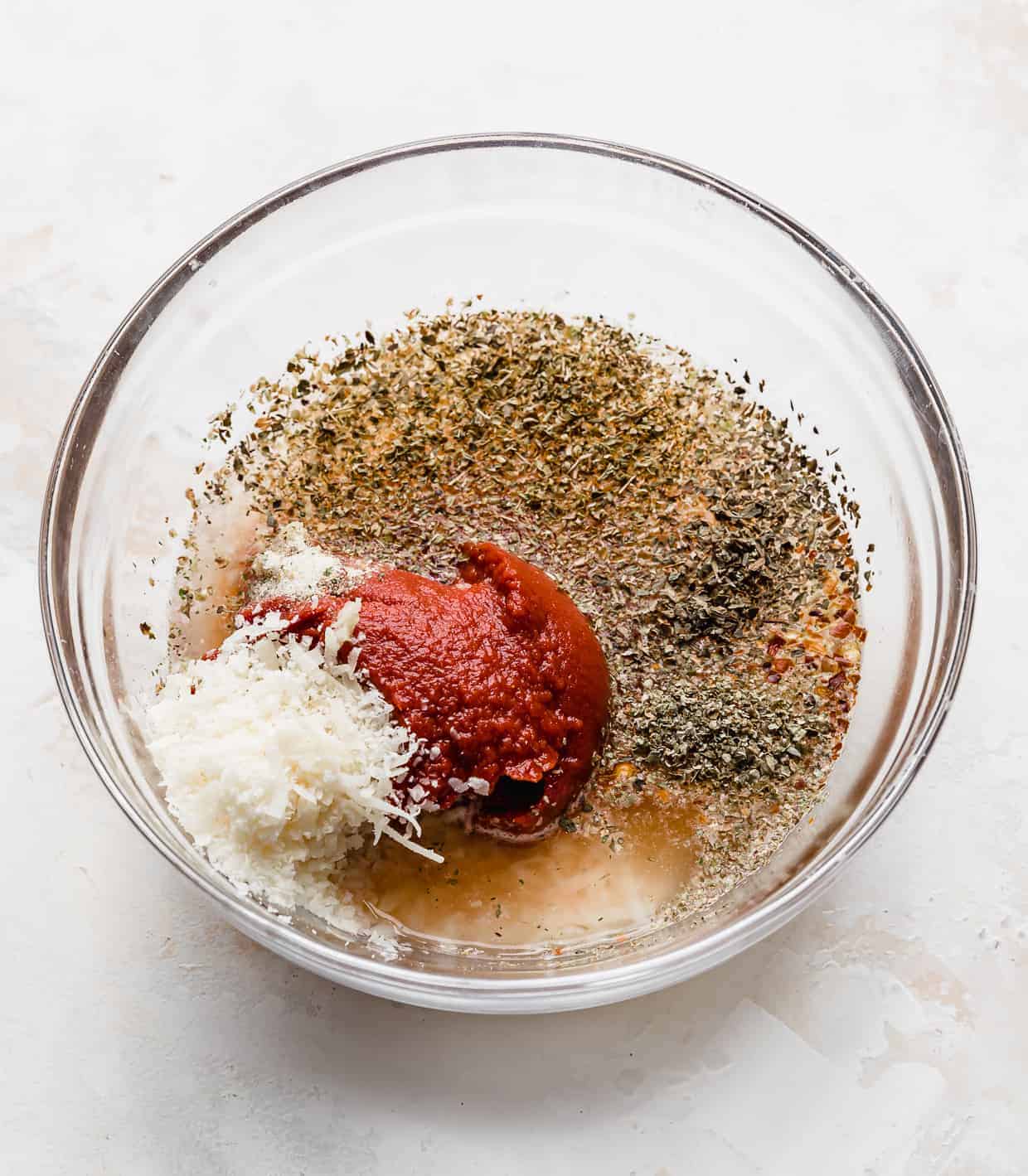 A glass bowl full of ingredients used to make pizza sauce from tomato paste.