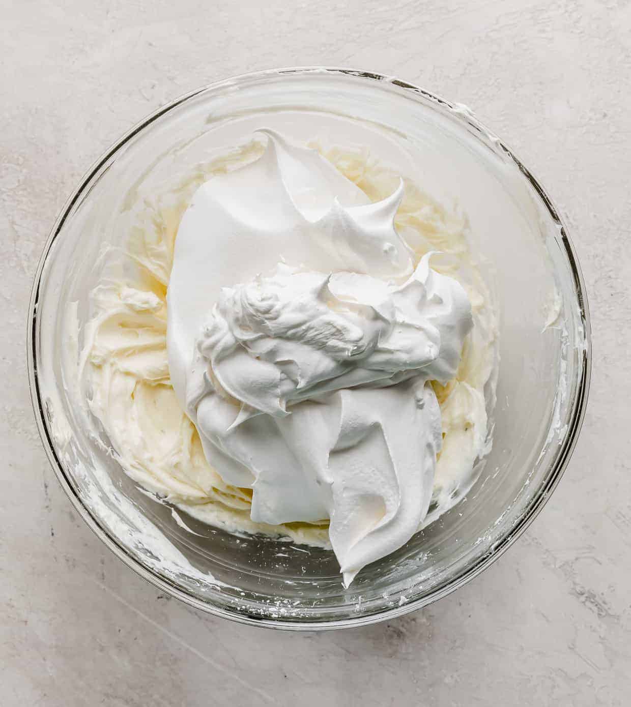 A large dollop of Cool Whip overtop a creamed cream cheese layer in a glass bowl.