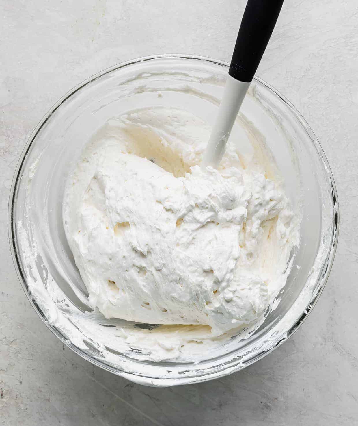 A glass bowl full of a white cream cheese and whipped cream mixture.