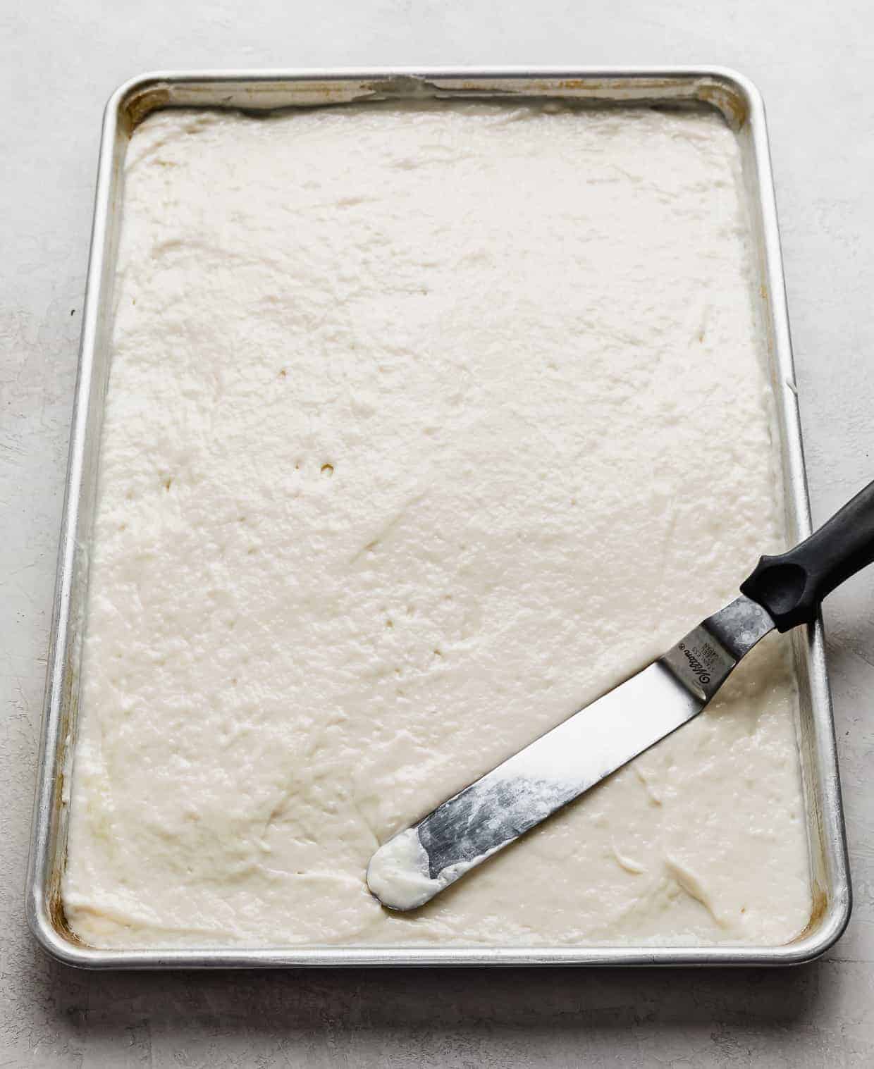 A baking sheet with white cake mix batter spread along the full sheet.