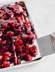 A metal spatula lifting up a slice of Raspberry Shortcake Sheet Cake from a baking sheet.