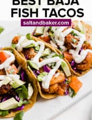 Baja Fish Tacos on a white plate topped with tomatoes and white sauce.
