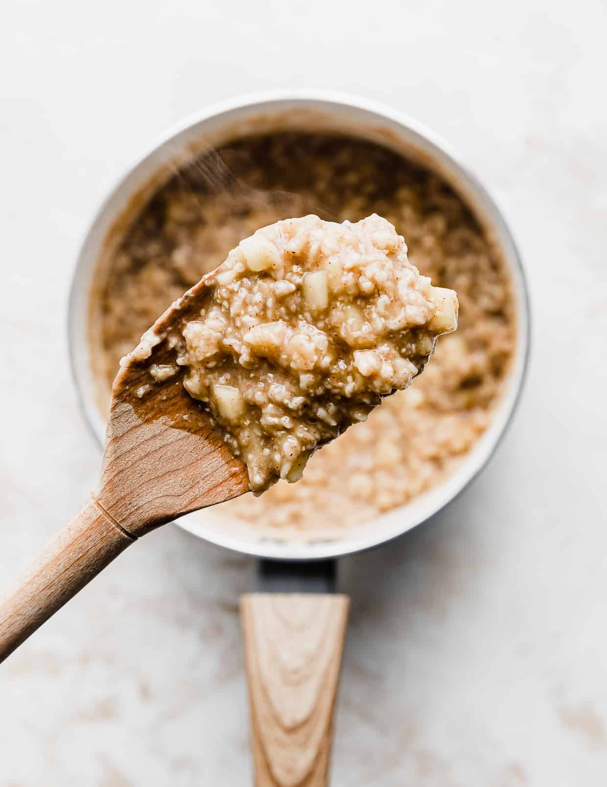 A wooden spoon hovering over a pot, holding up Apple Cinnamon Oatmeal.