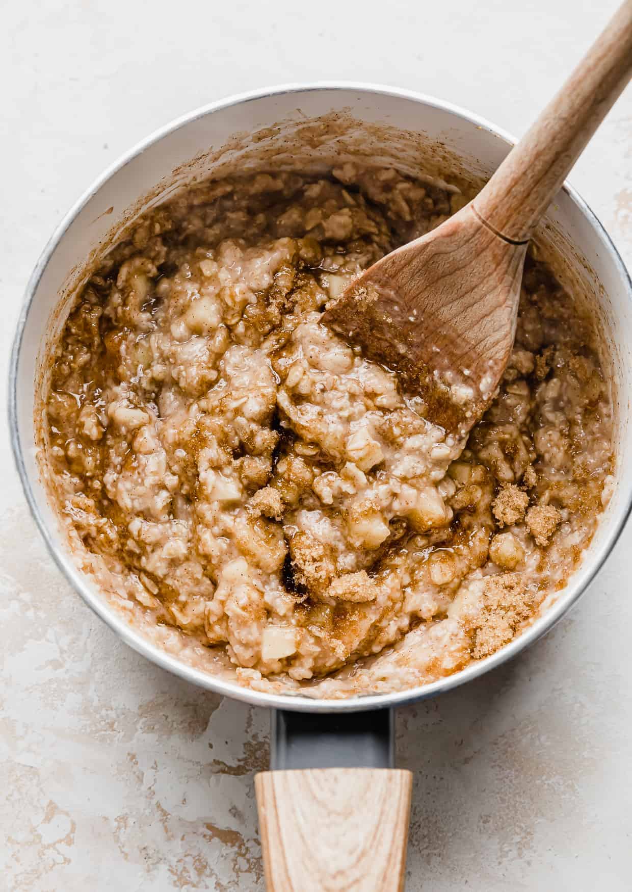 A wooden spoon stirring brown sugar into oatmeal in a pot. 