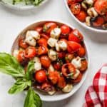 A white bowl full of sliced cherry tomatoes, mozzarella balls, and fresh basil drizzled with balsamic glaze.