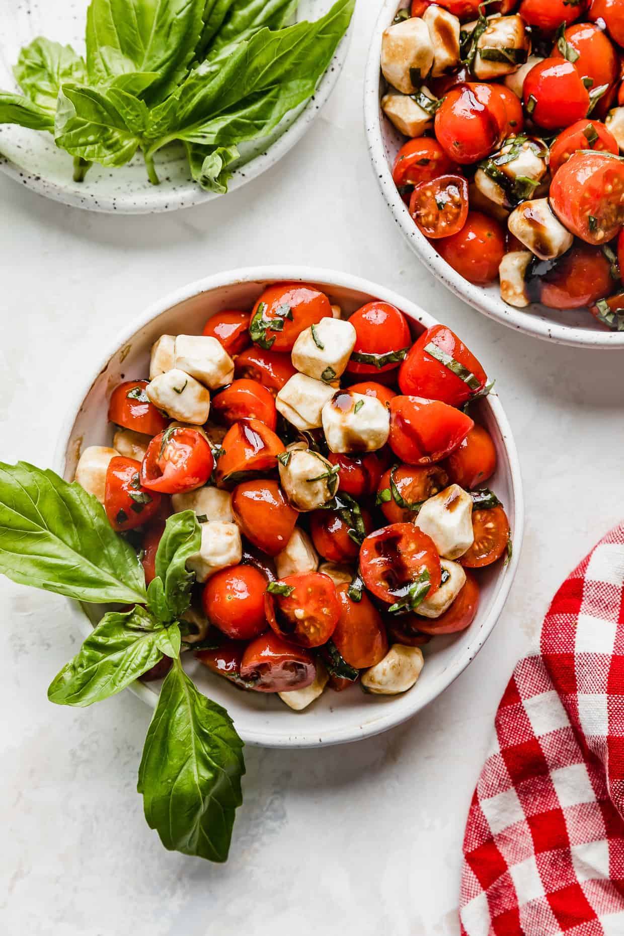 A white bowl full of sliced cherry tomatoes, mozzarella balls, and fresh basil drizzled with balsamic glaze. 