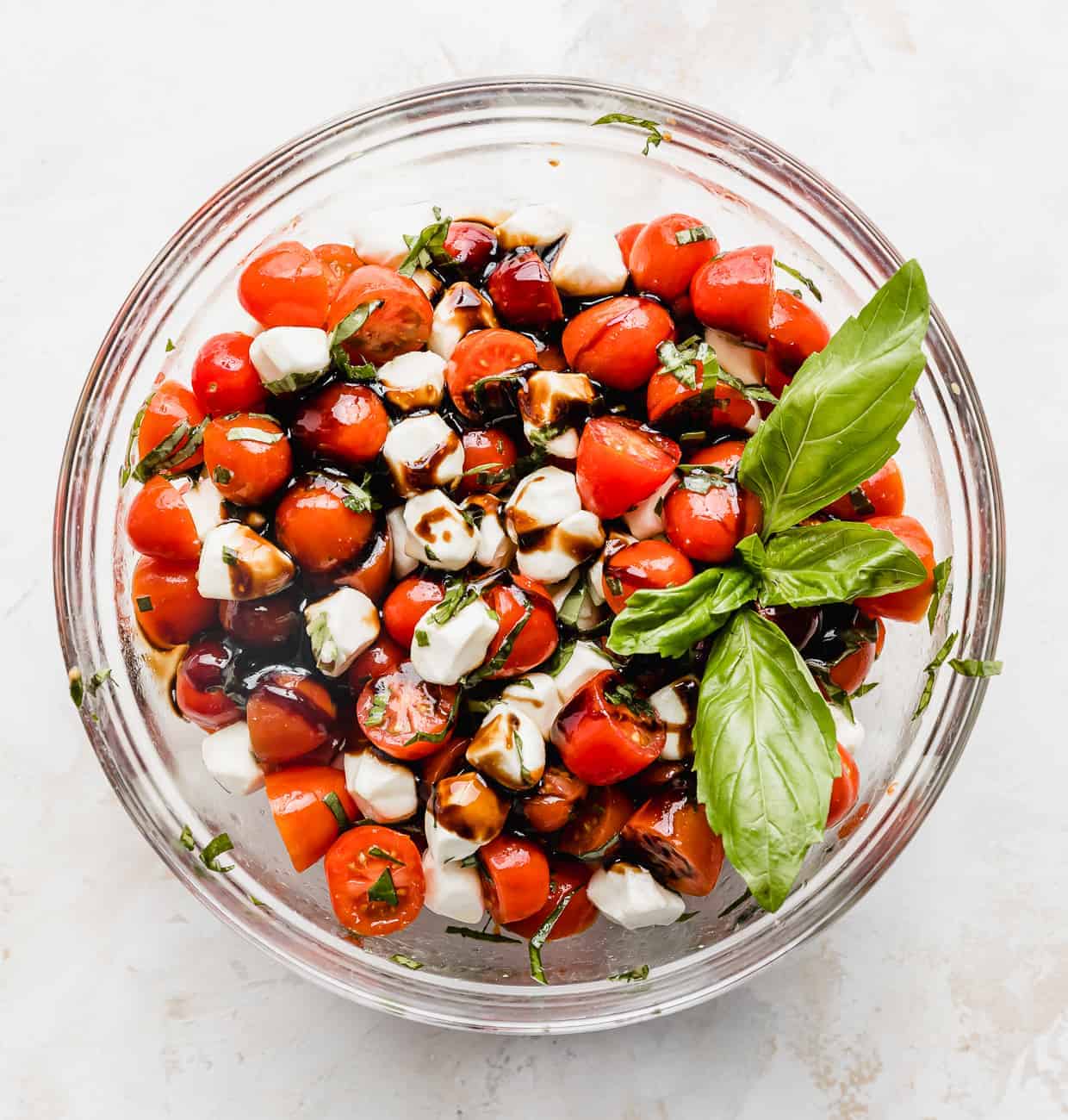 A cherry tomato caprese salad mixed with fresh mozzarella balls, fresh basil and a sprig of fresh basil on top.