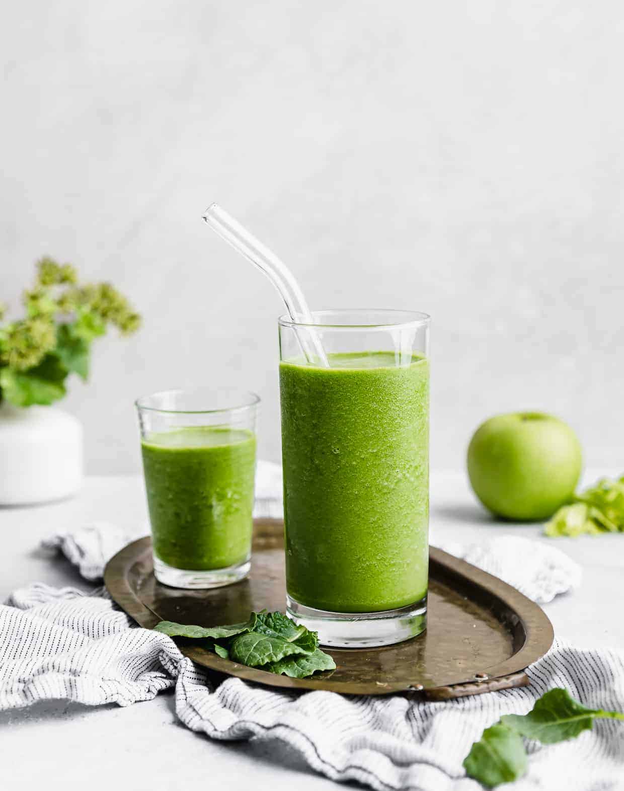 A clear glass full of bright green celery smoothie with a glass straw in the cup. 
