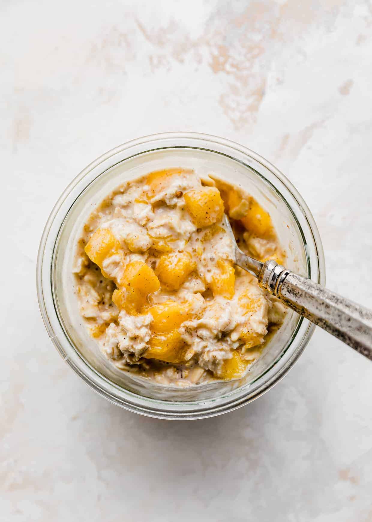 Overhead photo of a spoon scooping into mango overnight oats with cinnamon and nutmeg. 