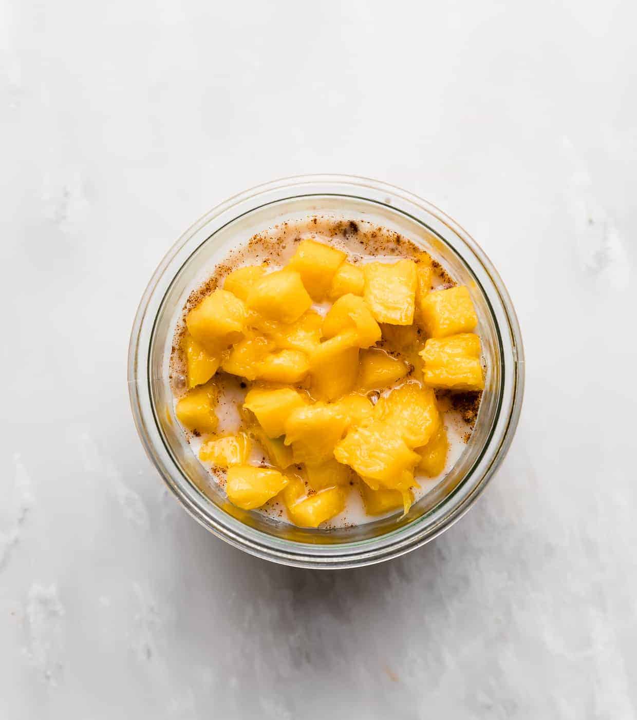 Diced mango overtop of a milk and oat mixture in a glass jar.