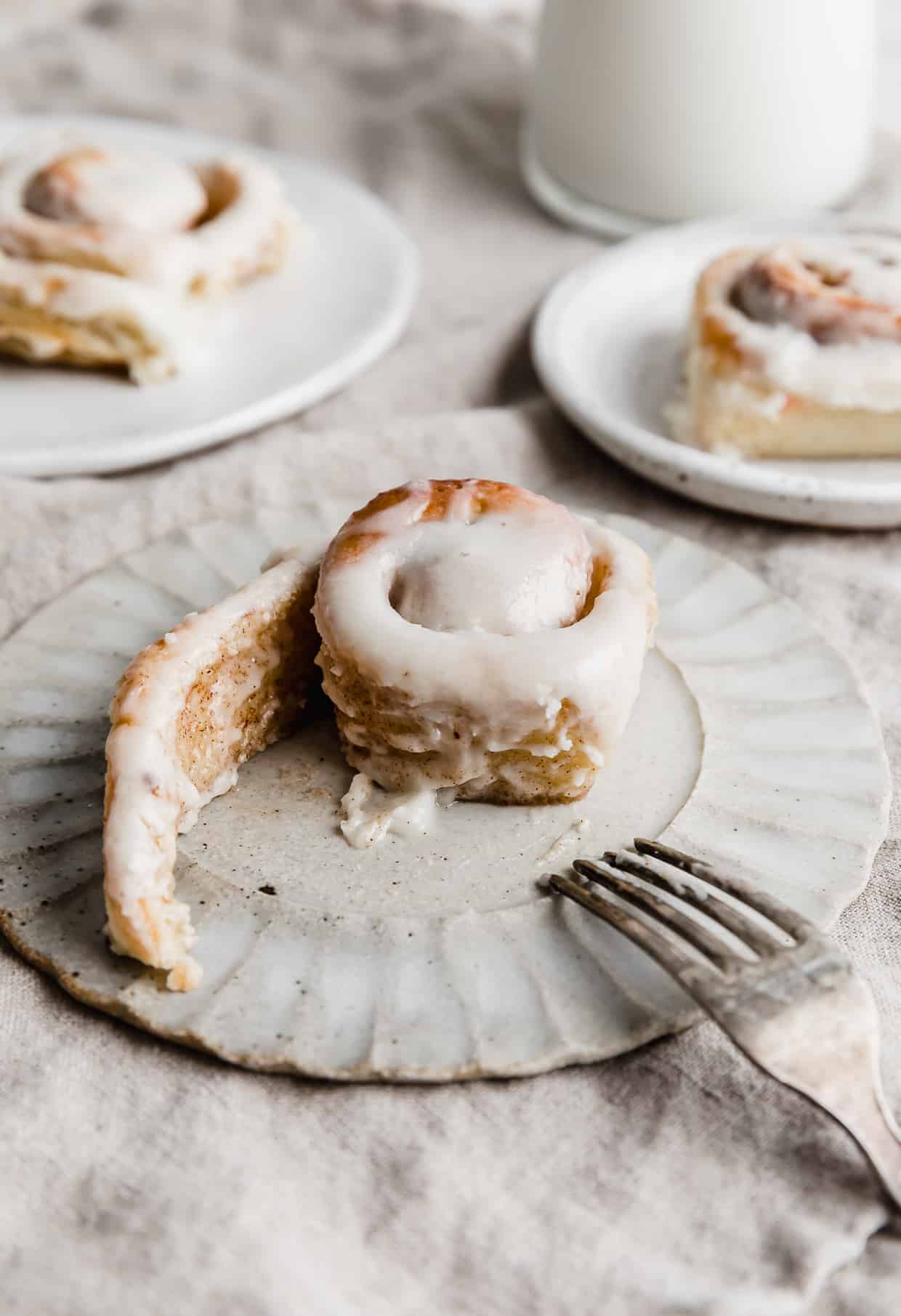 A mini cinnamon roll on a plate with the tail of the roll unraveled. 
