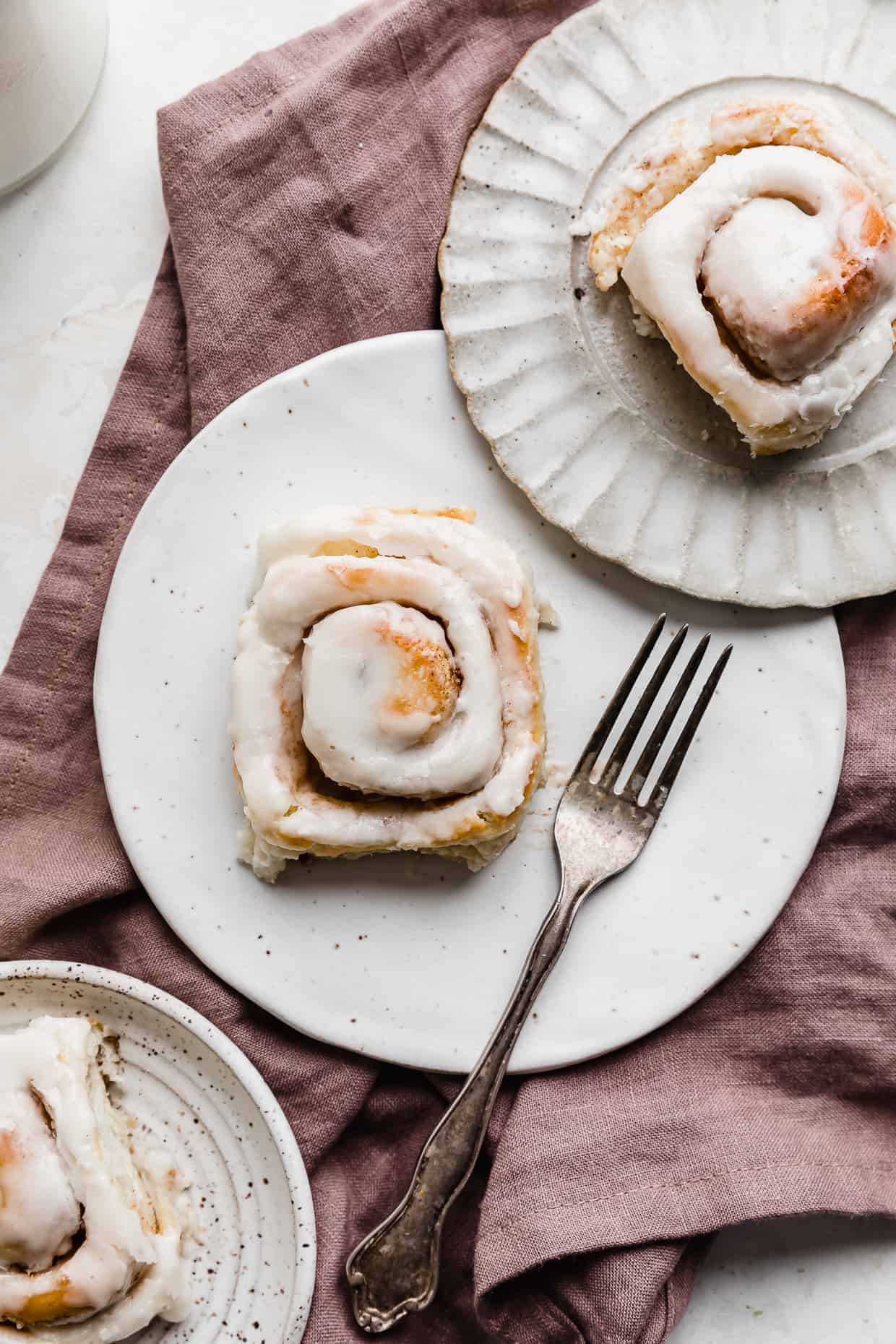 A mini cinnamon roll on a white plate that's on a lilac linen napkin.