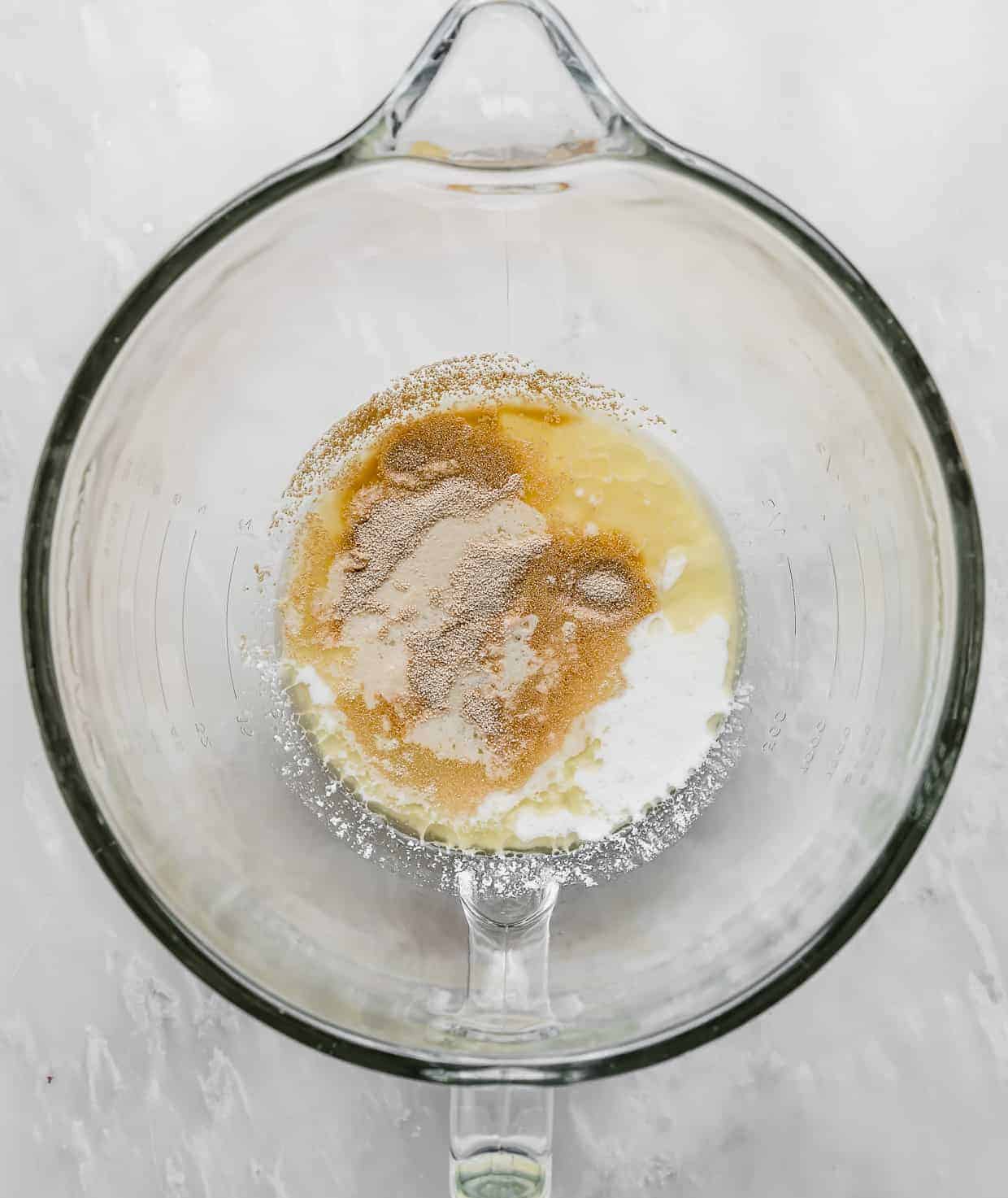 A glass mixing bowl with yeast, buttermilk, butter, and water in it.