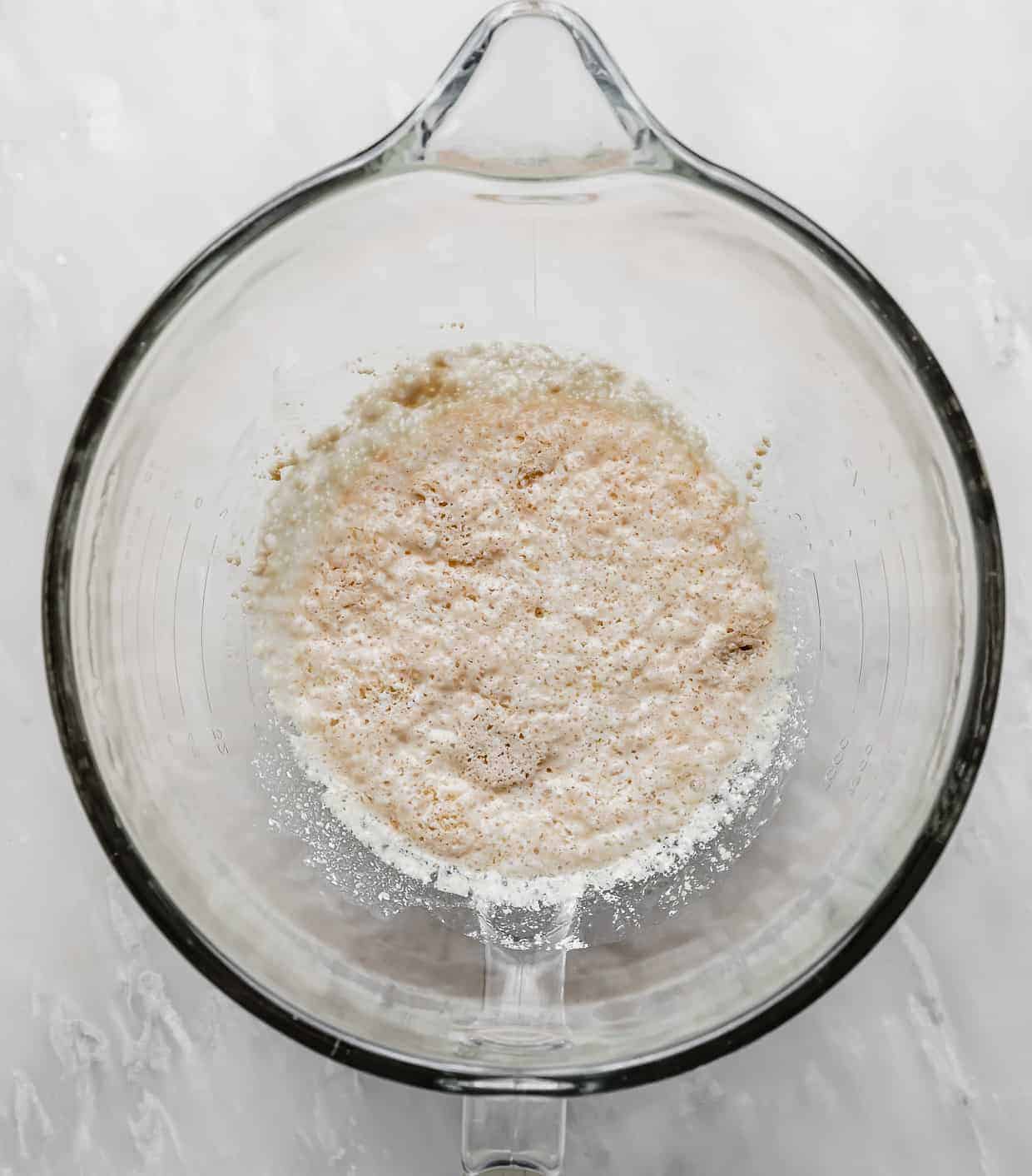 A foamy yeast mixture in a glass stand mixer bowl.