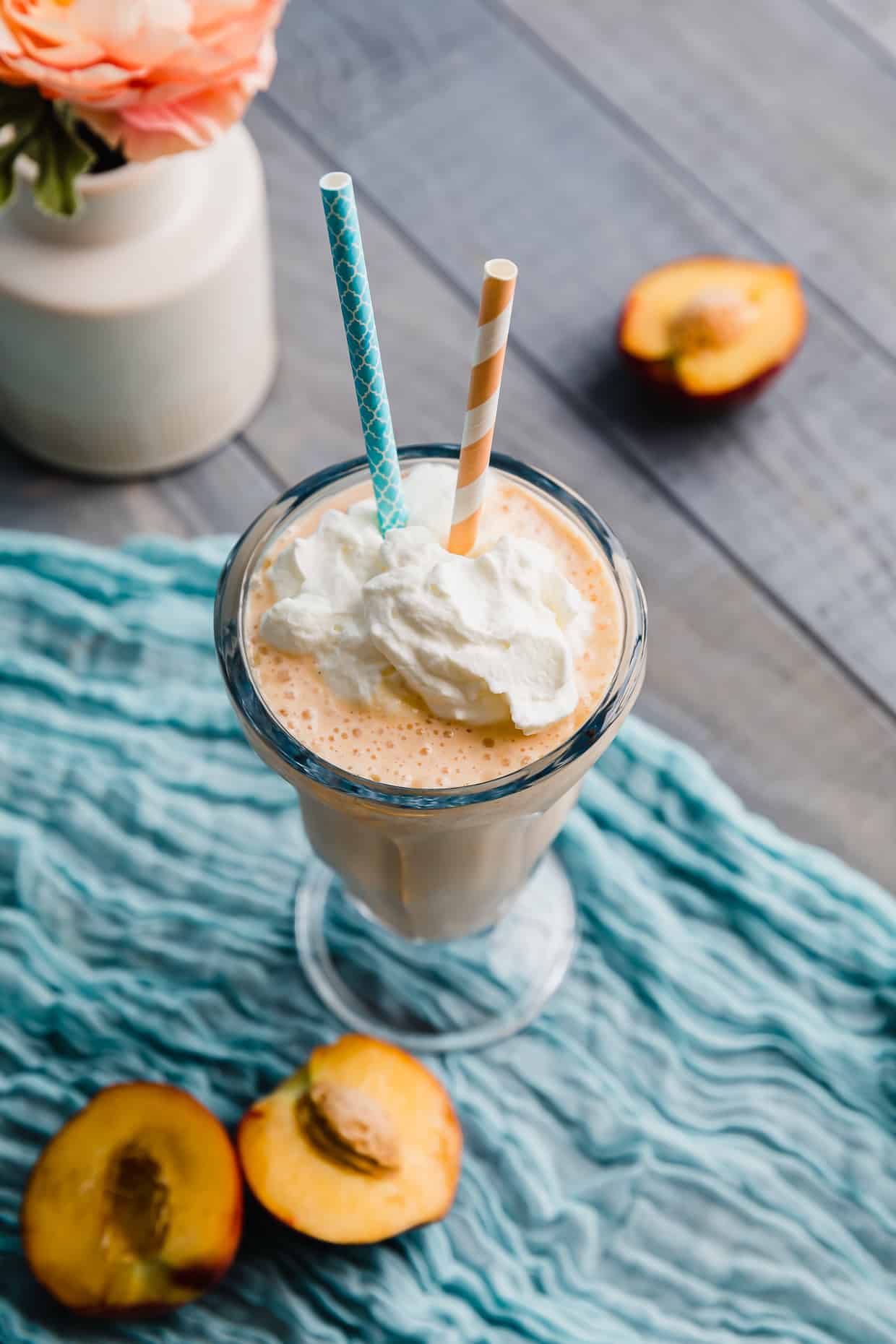 A Peach Milkshake on a blue napkin with two straws in the glass.