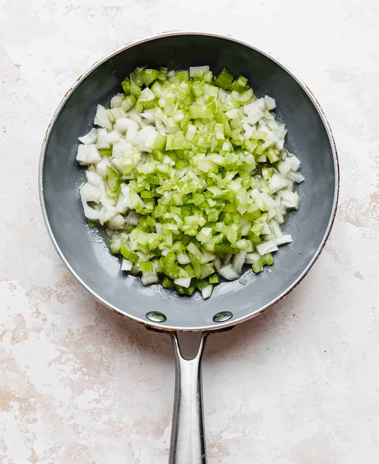 A gray skillet with diced onion and diced celery in it.