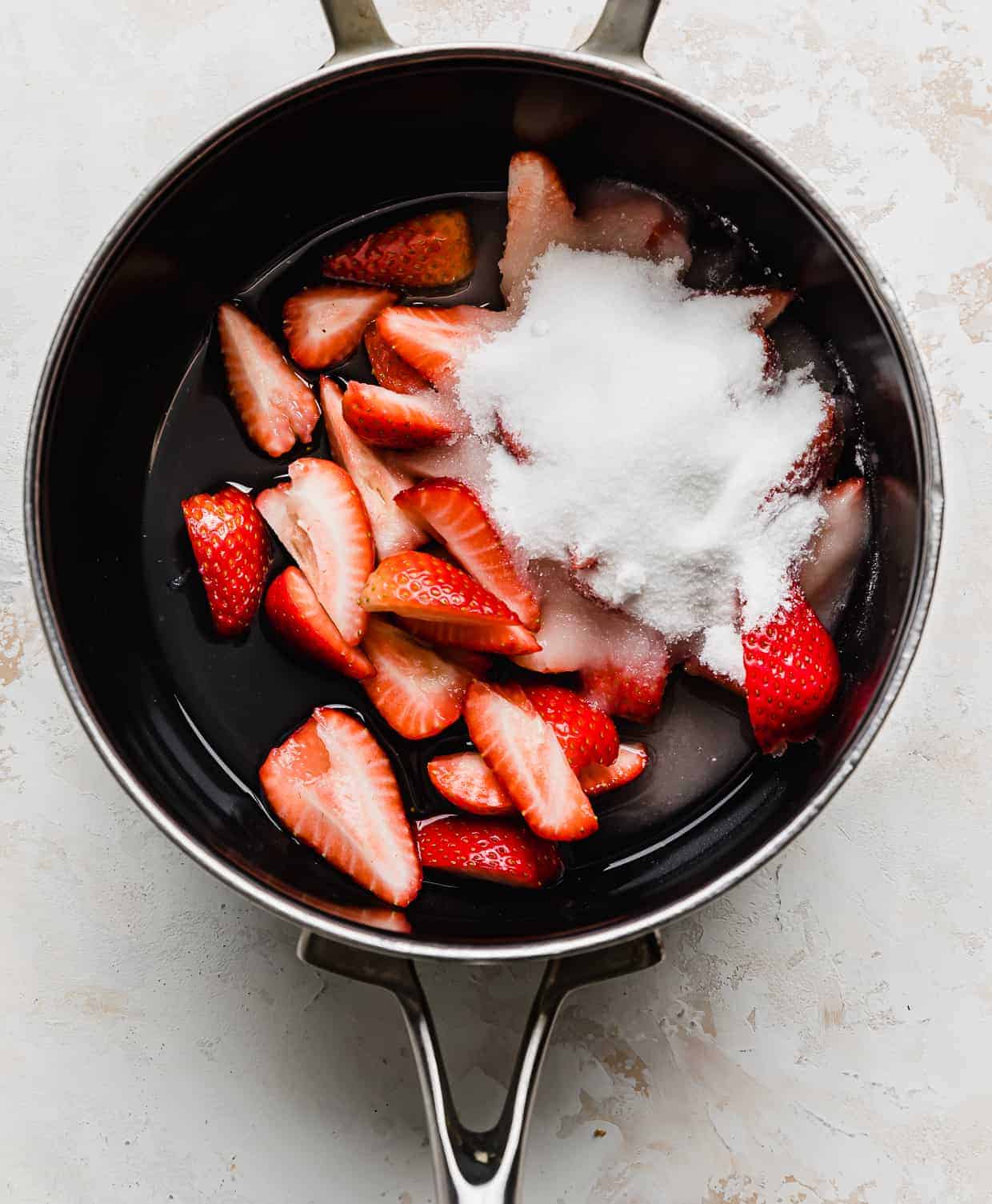 Quartered strawberries and sugar in a saucepan.
