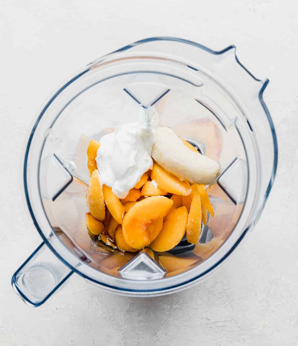 Overhead photo of a blender filled with frozen peach slices, yogurt, banana, milk, and honey.