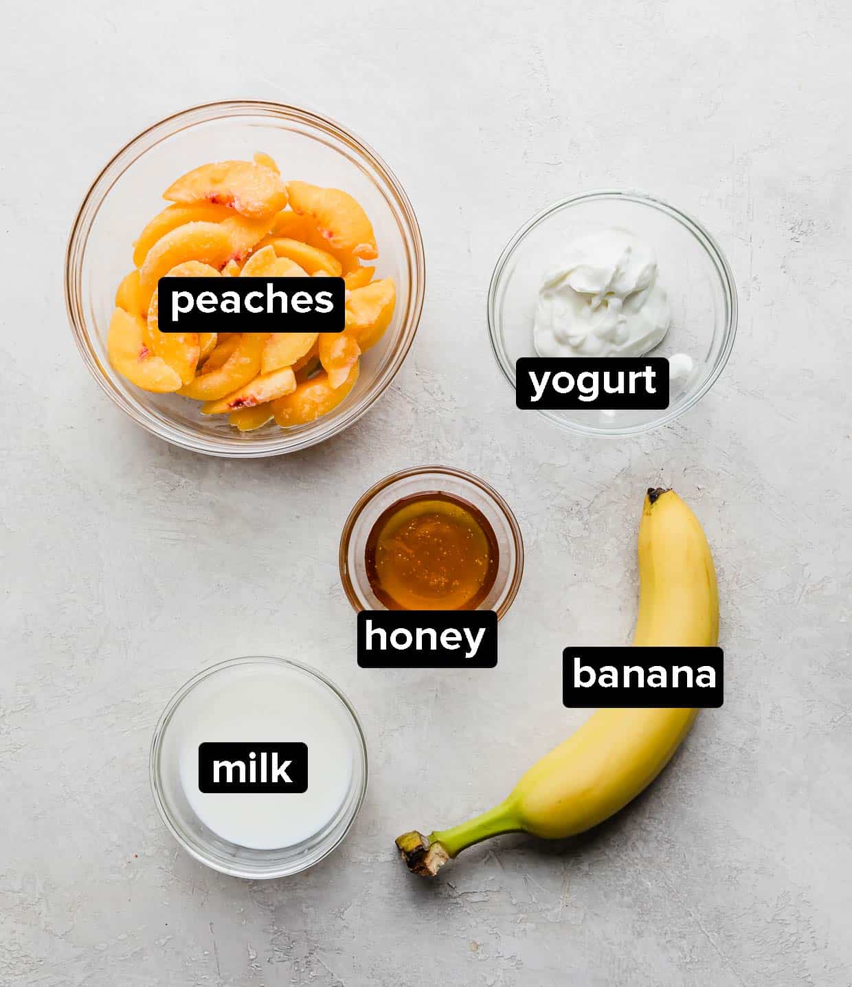 Ingredients used to make a banana peach smoothie on a gray background.