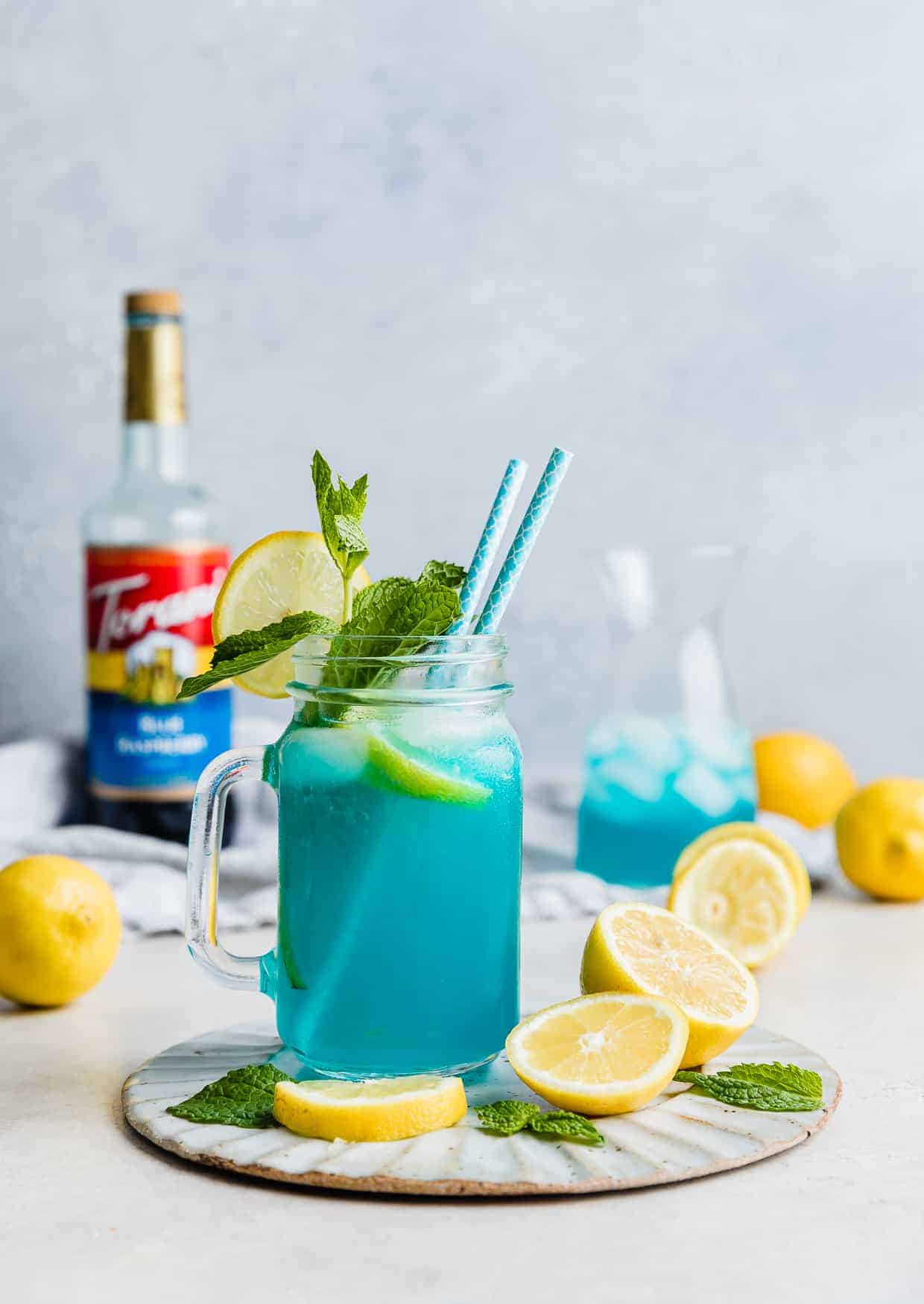 A Blue Raspberry Lemonade in a glass jar with sliced lemons in the background.