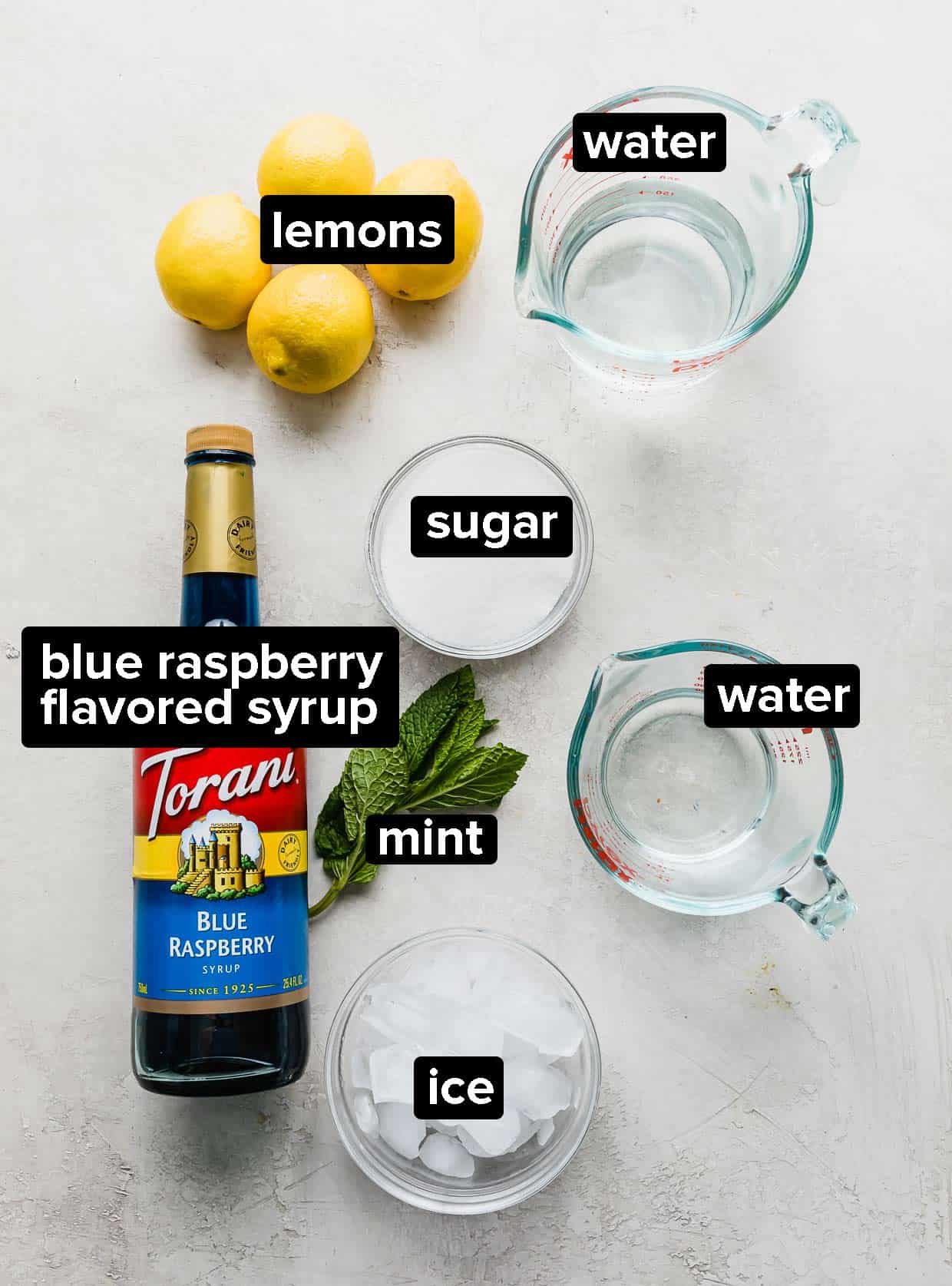 Ingredients used to make blue raspberry lemonade on a gray and white background.