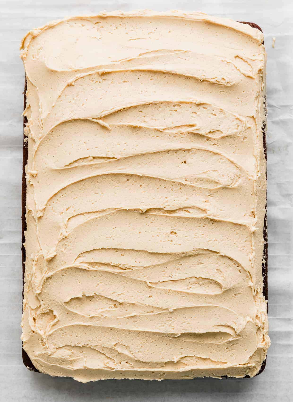 A light golden colored peanut butter frosting spread across a sheet chocolate cake.