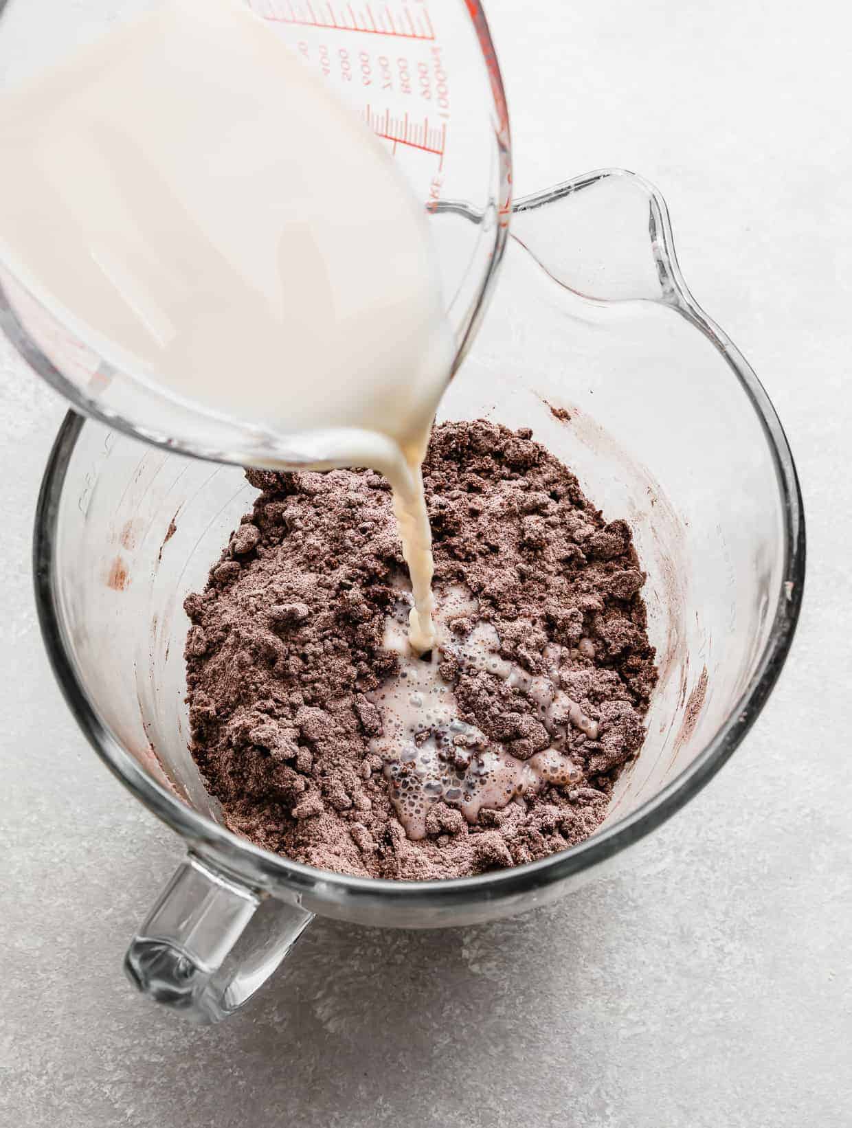 A white liquid being poured into a bowl with chocolate cake dry ingredients.