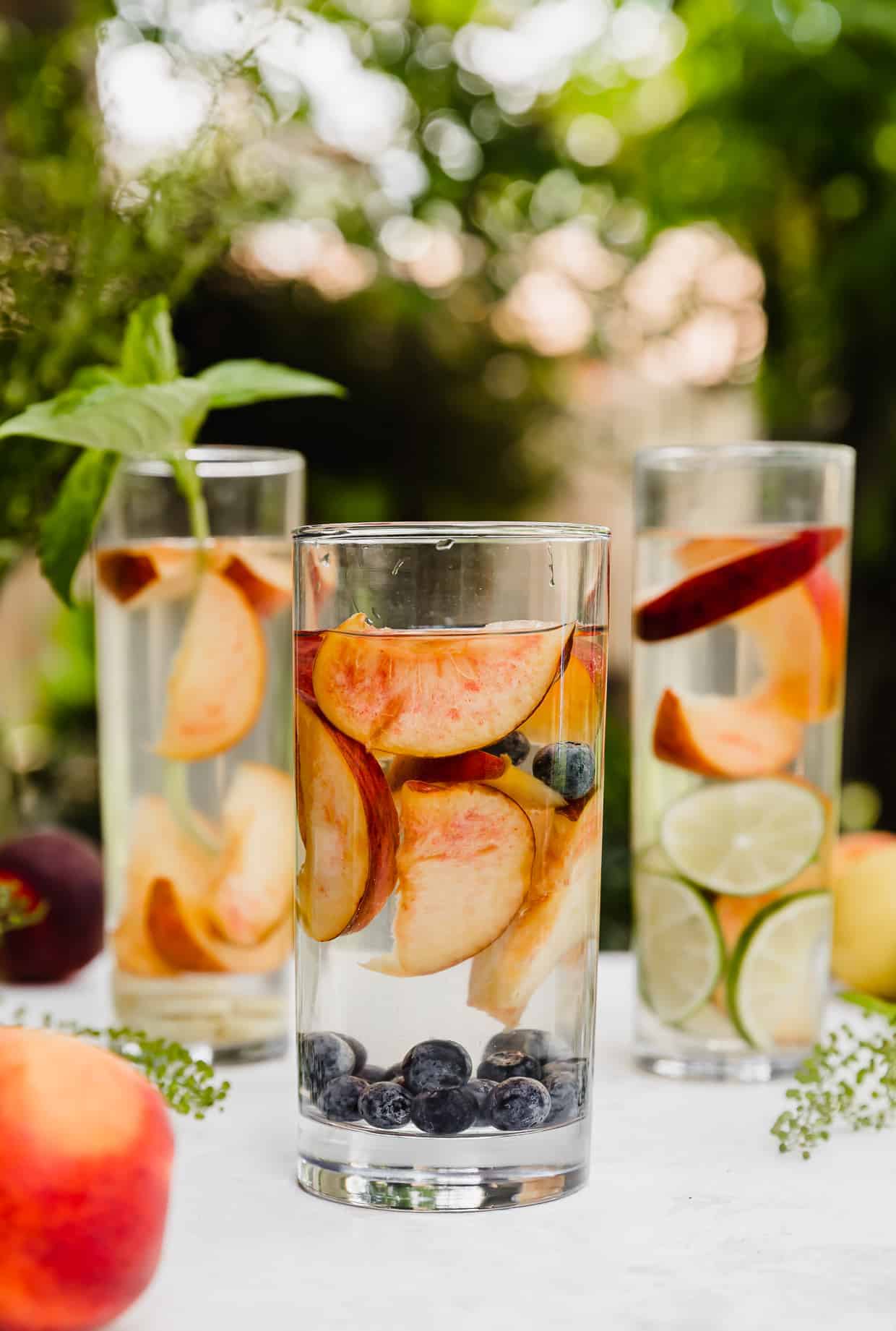 A glass of water full of sliced peaches and fresh blueberries.