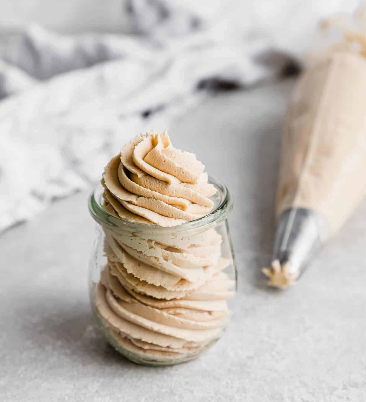 Peanut Butter Frosting piped into a small glass jar on a white background.