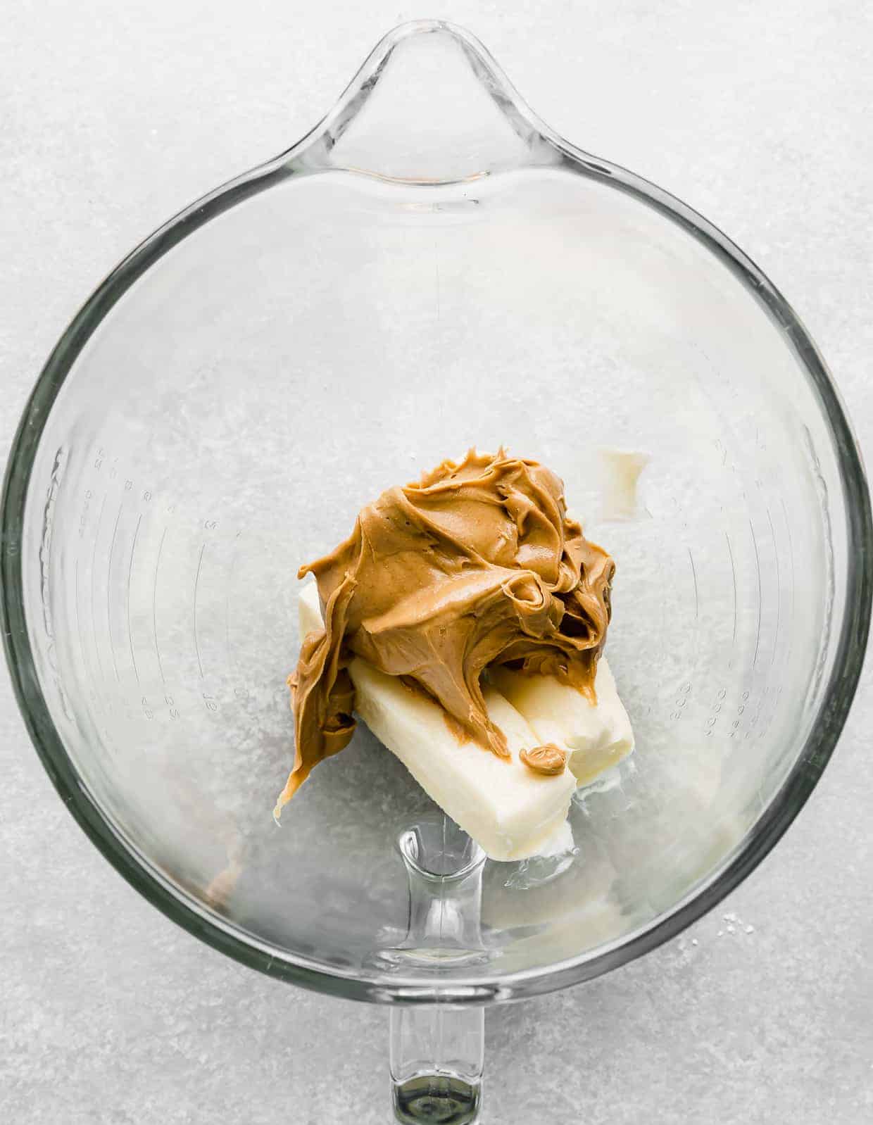 A glass stand mixer bowl with butter and peanut butter in it.