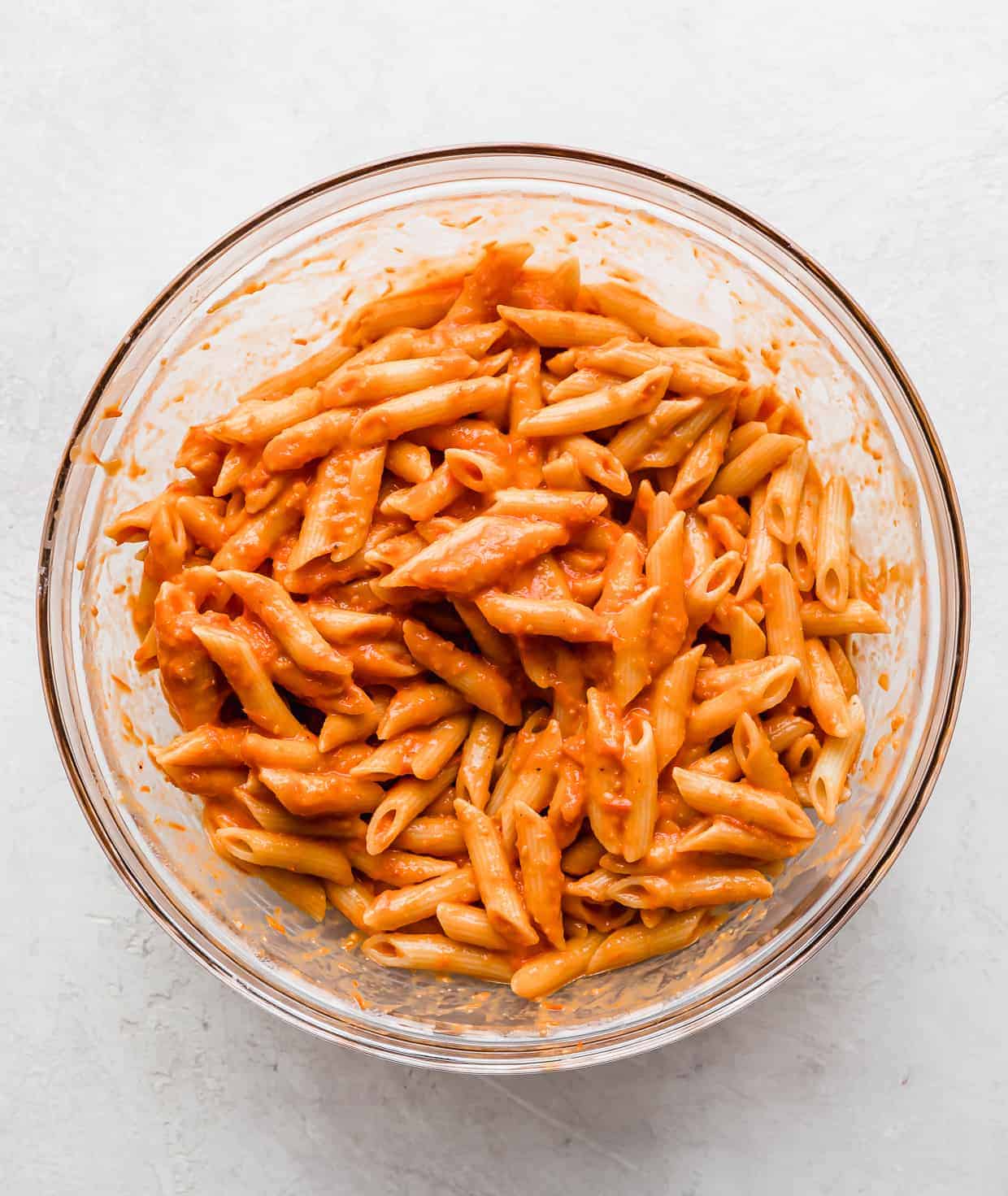 Cooked penne noodles tossed in a red sauce in a glass bowl.