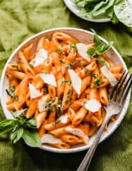 A white plate full of red Penne Pomodoro pasta topped with fresh basil.