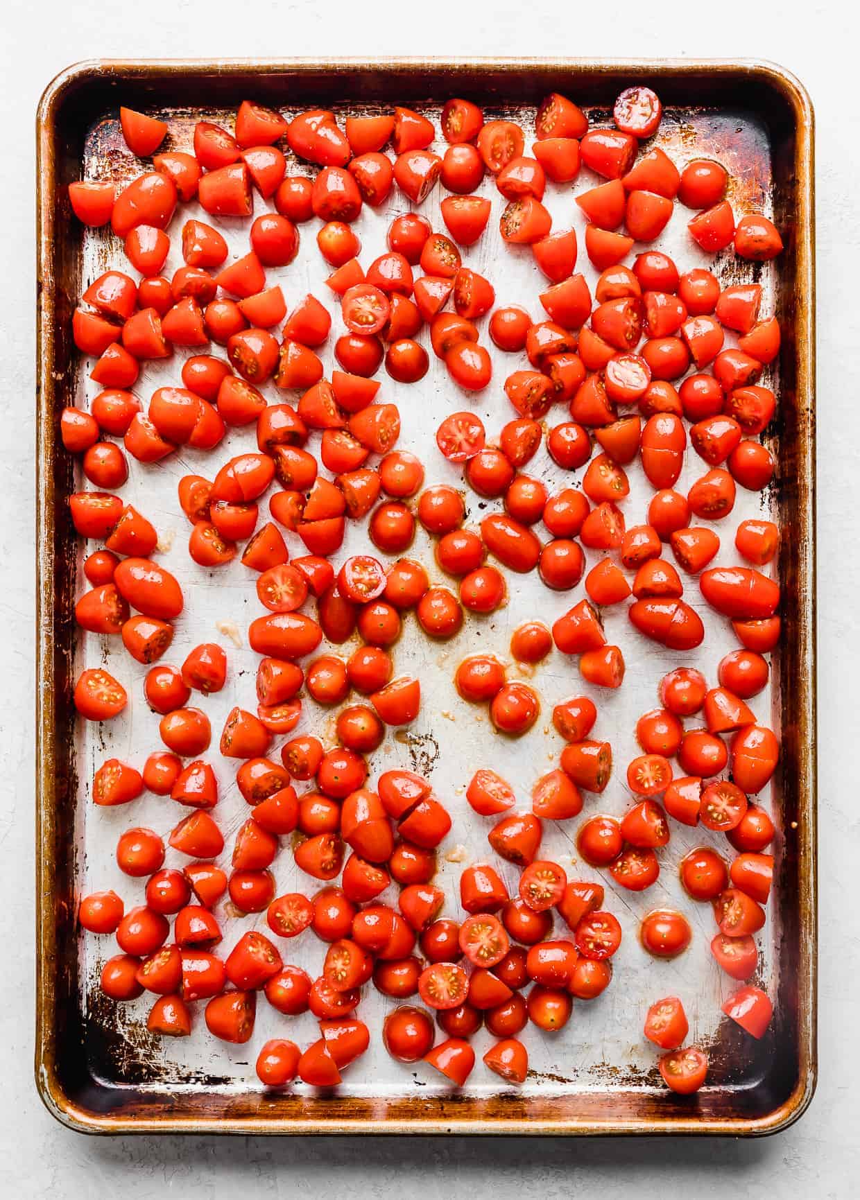 Sliced small tomatoes on a baking sheet spread into a single even layer.