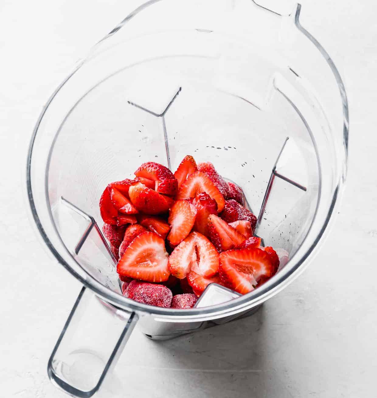 Fresh and frozen strawberries in a blender on a white background.