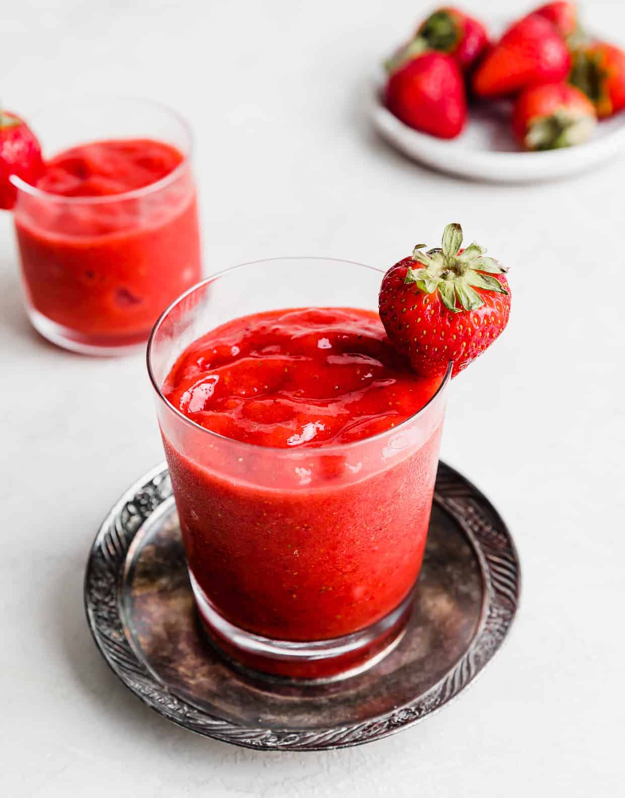 A glass cup with Virgin Strawberry Daiquiri in it with a full strawberry garnish on the brim.