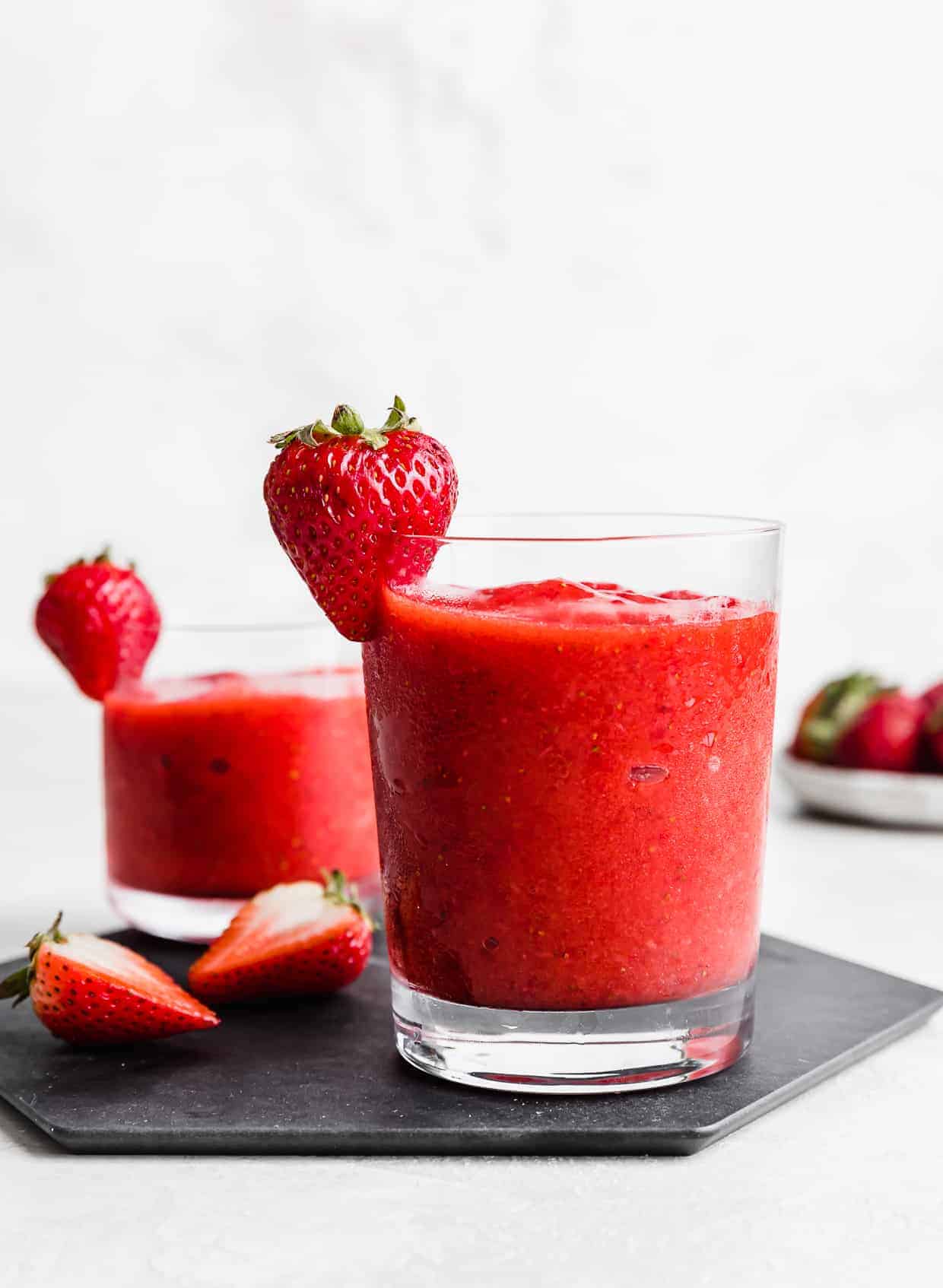 A glass of red non alcoholic strawberry daiquiri on a black plate against a white background.