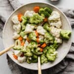 A bowl full of steamed and buttered broccoli, cauliflower, and carrots.