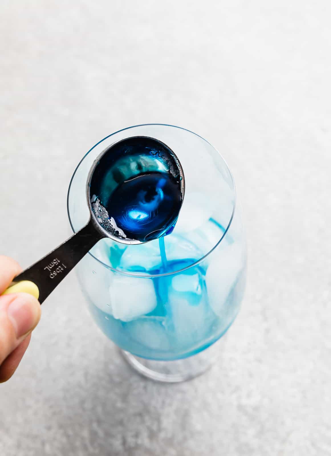 A tablespoon full of blue curaçao syrup being poured into a glass cup.