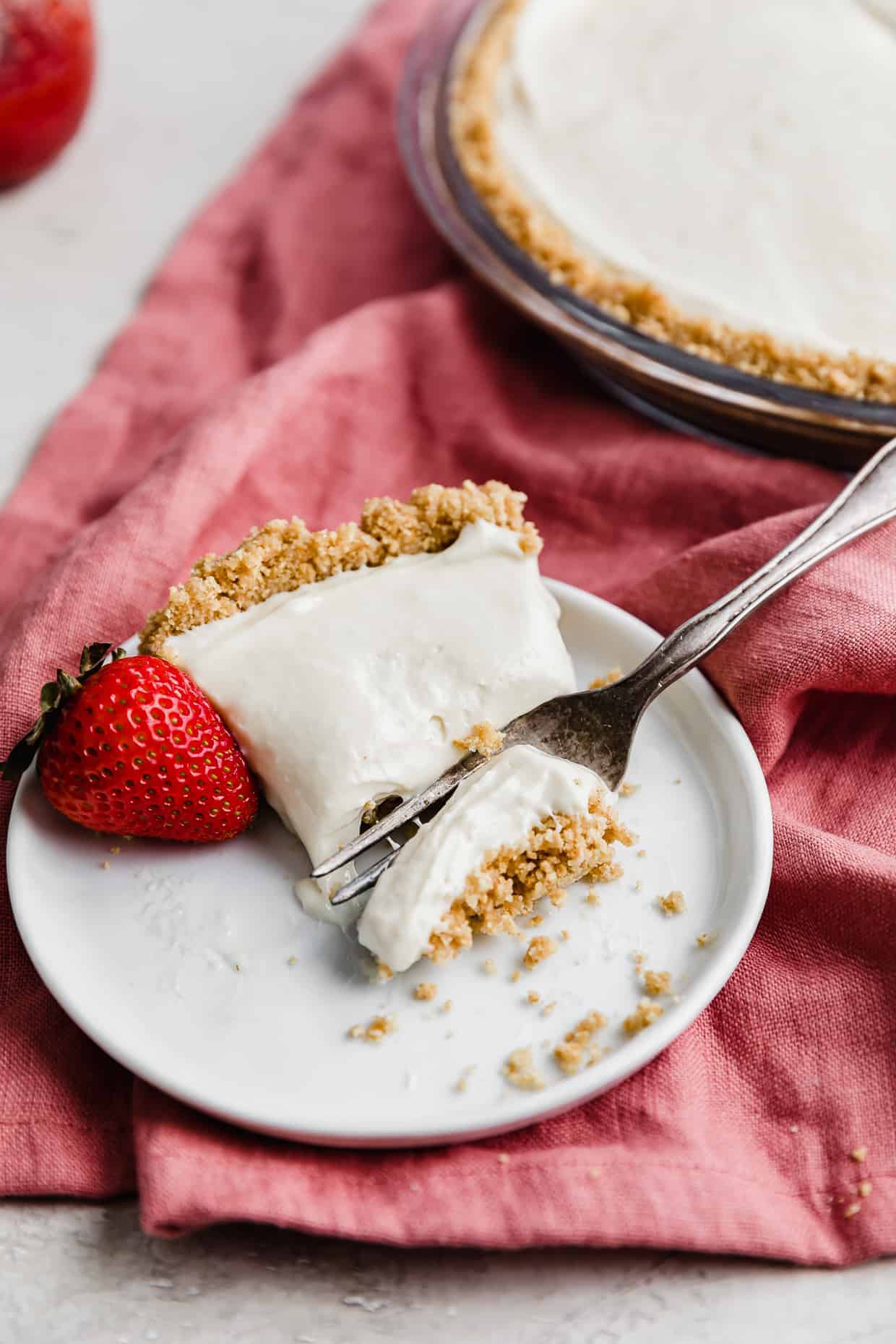 A slice of no-bake cheesecake on a white plate with a fresh strawberry to the side.